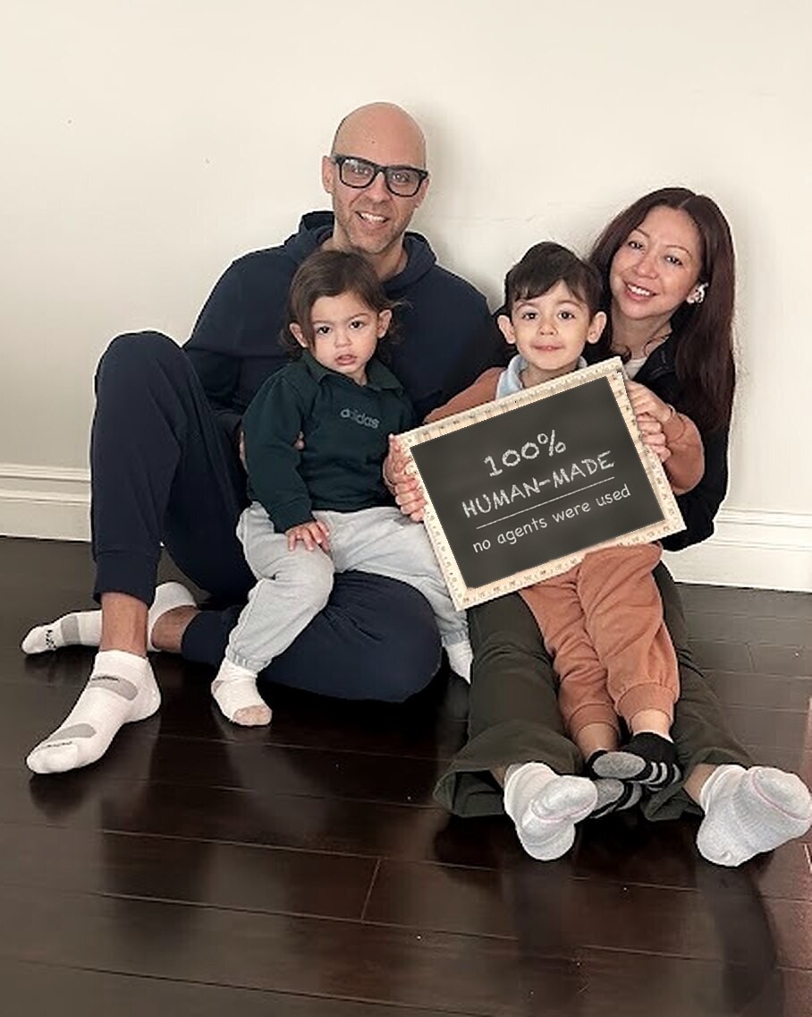 Kalvin and Jacqueline sitting on the floor at home with their two kids, holding a chalkboard that reads: 100% human-made, no agents were used